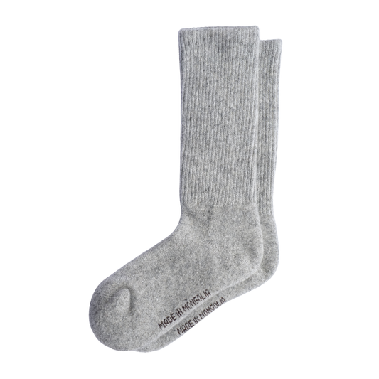 Une paire de chaussettes en laine côtelée gris clair présentée sur un fond blanc uni, avec la mention « MADE IN MONGOLIA » imprimée sur la semelle.