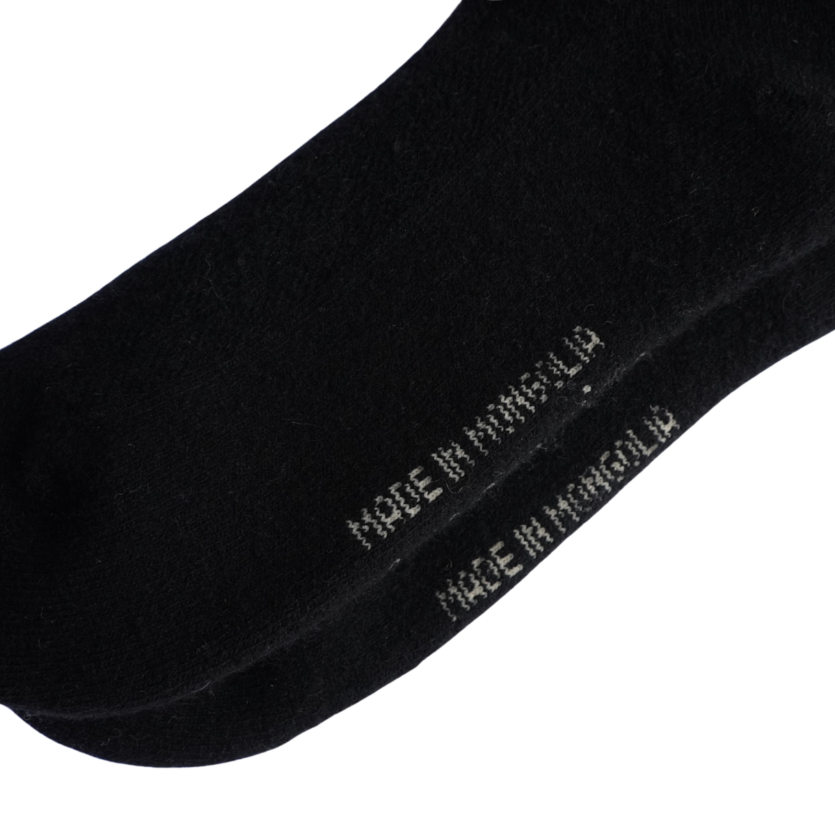 Gros plan sur une chaussette noire avec la mention « MADE IN MINSOLID » brodée en blanc sur le côté, présentée sur un fond blanc uni.